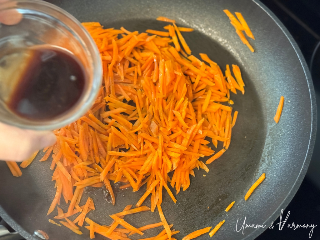Soy sauce seasoning mixture being added to sautéed carrots