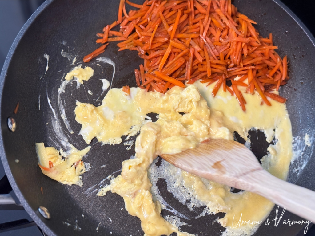 Egg cooking on one side of the pan while carrots are pushed aside