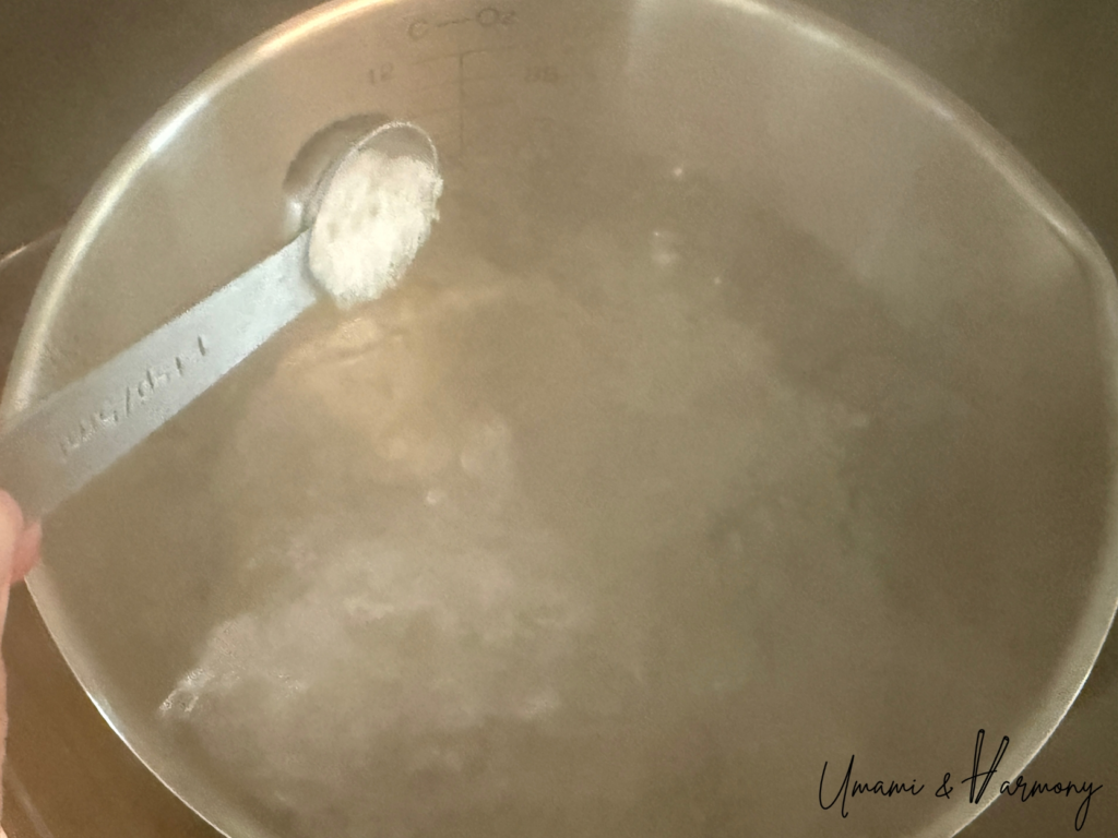 A teaspoon of salt being added to a pot of boiling water