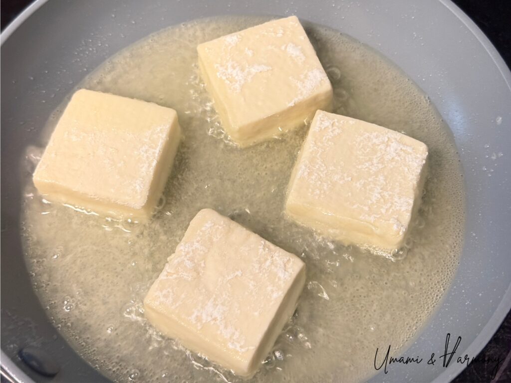 Tofu being fried in a pan until lightly golden