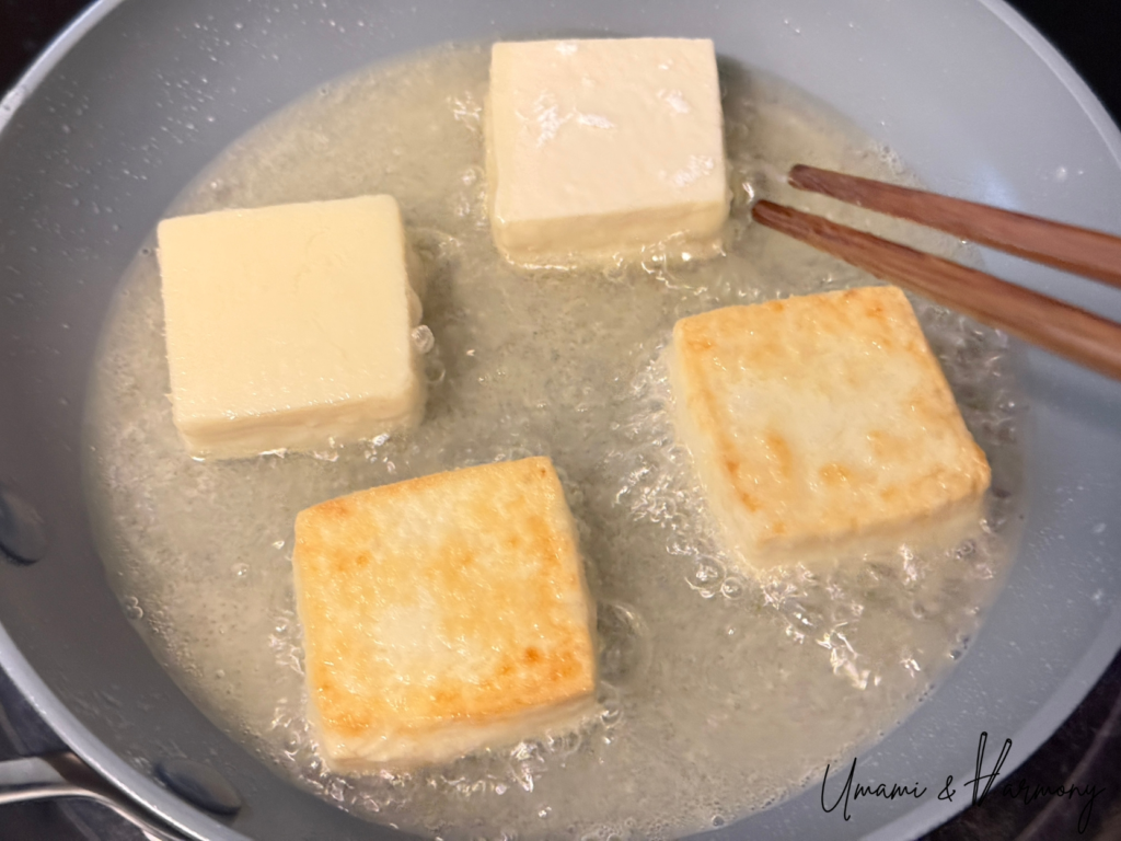 Fried tofu being turned gently in hot oil