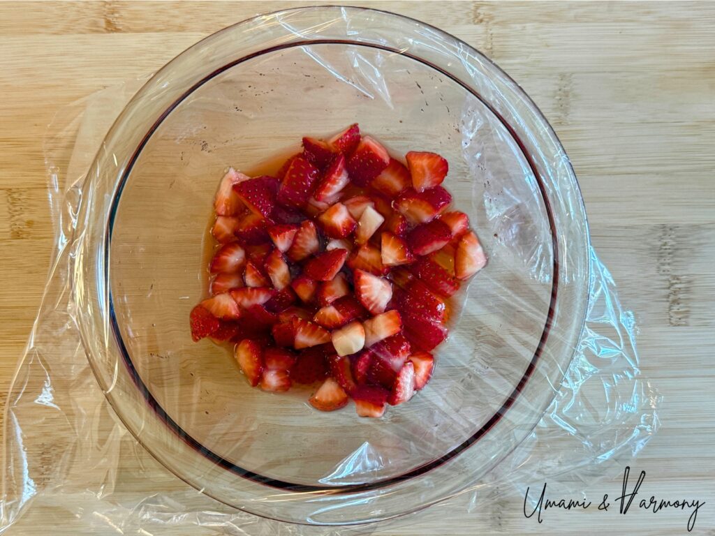 Strawberry mixture in a glass bowl covered with plastic wrap before microwaving