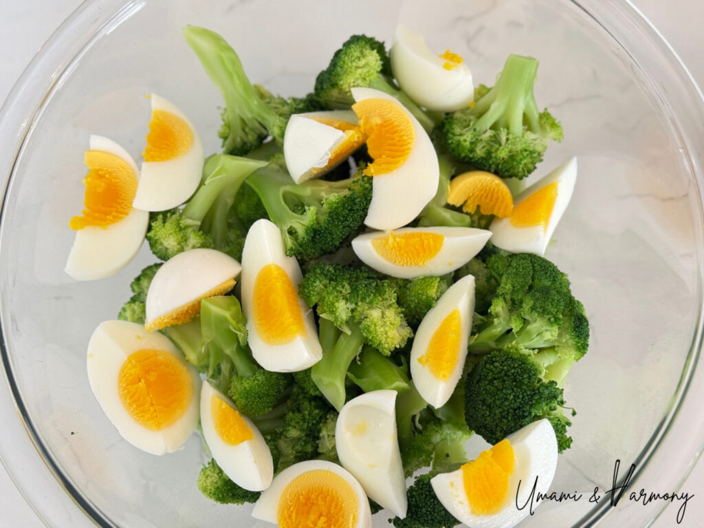 Hard-boiled eggs and broccoli florets are added in a mixing bowl