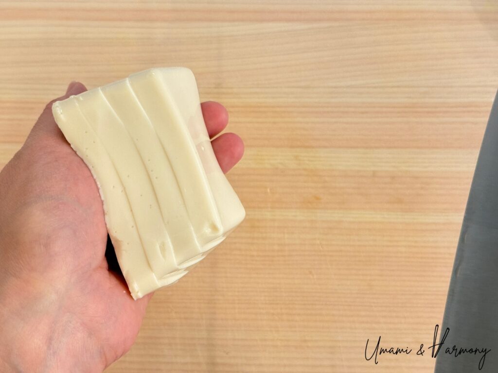 Silken tofu being gently cut into cubes on the palm of a hand