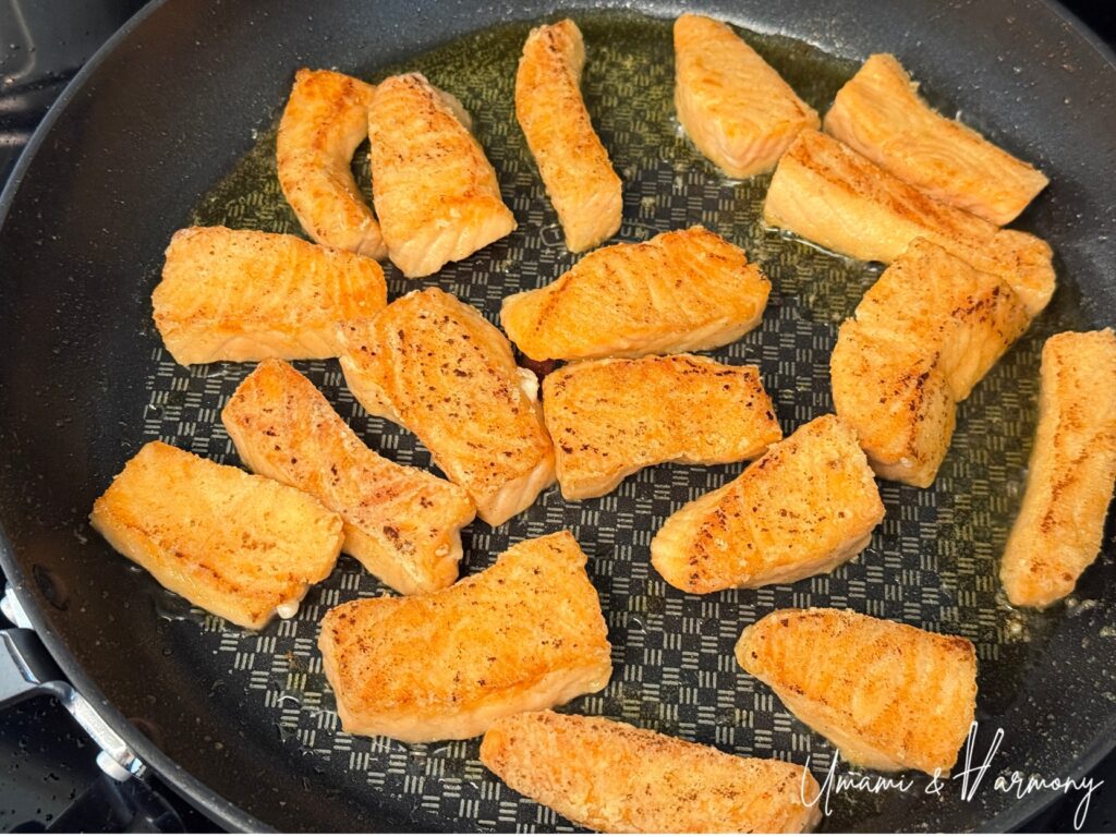 Salmon pieces being pan-fried in a skillet